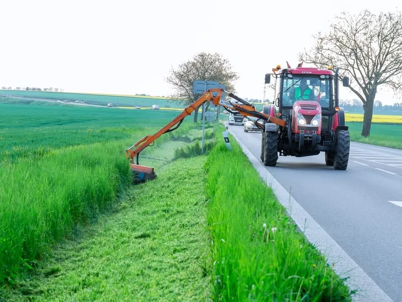 Tracteur équipé d'un bras de fauchage entretenant le bord d'une route rurale